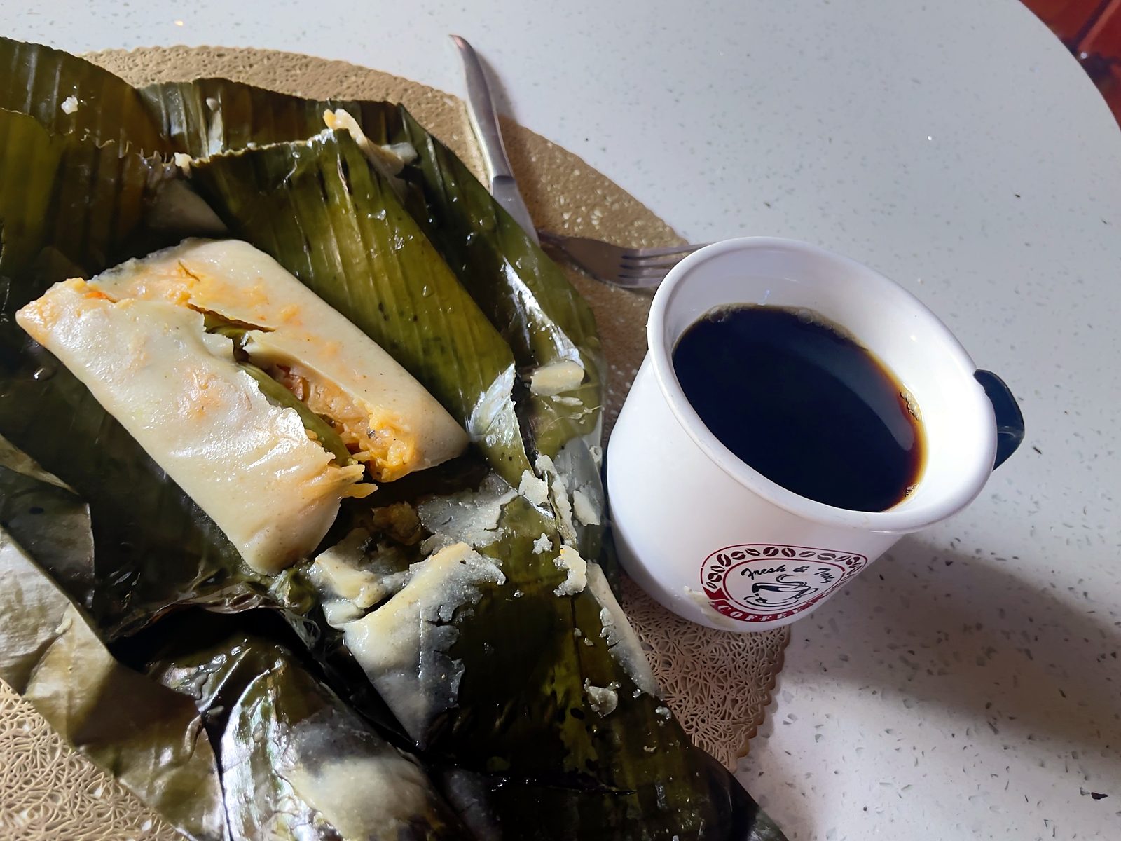 Um tamal costarriquenho em folhas de bananeira com uma xícara de café preto