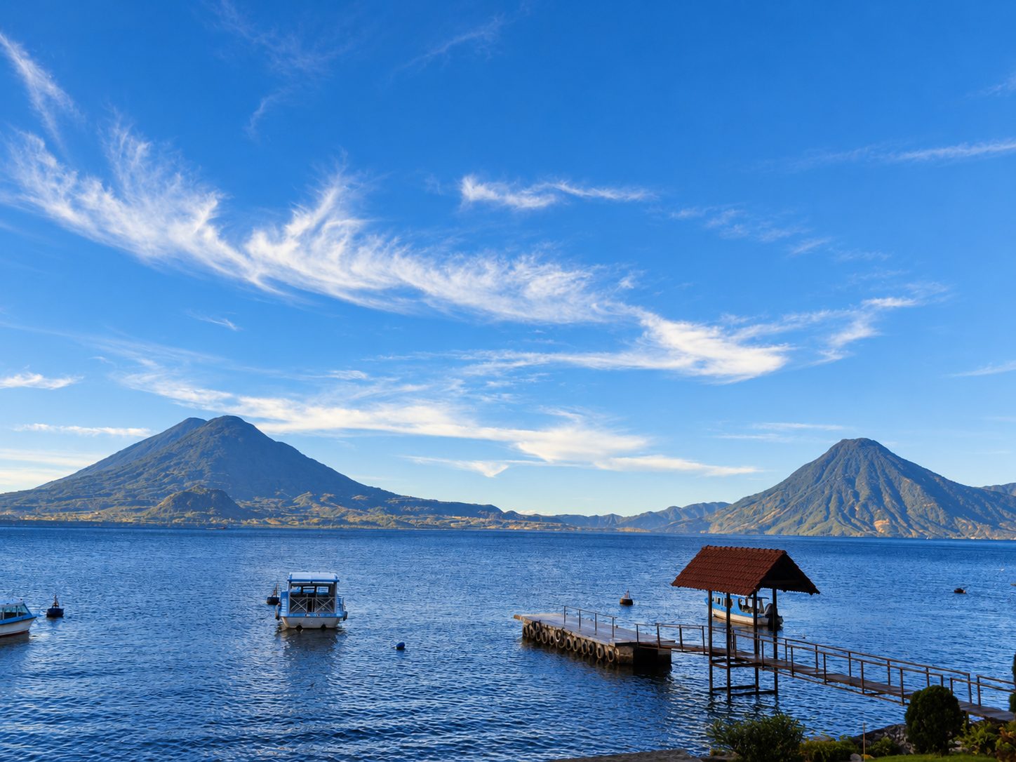 Il Lago Atitlán con barche, un pontile e due vulcani alle spalle